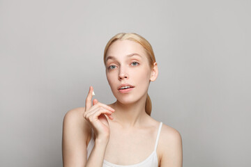Portrait of pretty woman with blonde hair holding white moisturizing cream on her finger isolated on grey