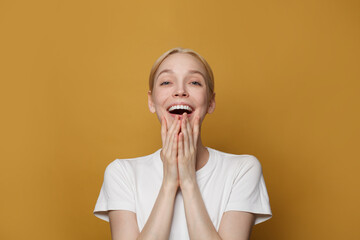 Beautiful amazed woman in t-shirt looking at camera. Studio shot of charming surprised lady isolated against yellow studio wall background.