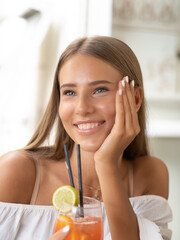 A young woman is enjoying a cocktail with a smile
