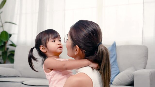 4K, Beautiful Asian mom, holding a beautiful little girl in she arms, daughter hugged mother's neck, two sat together in living room, mother kissed daughter's cheek several times, so cute and warm.