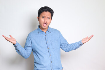 Portrait of Asian man in blue shirt spreading hands, choosing between 2 different options, holding two hands with empty space. Decision and choice concept. Isolated image on white background