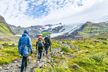 Fototapeta na wymiar Group of tourists walking on narrow path to glacier for glacier tour and expedition. Tour members wearing helmet and full gear to climb glacier. Glacier, ice and mounts ins in background.