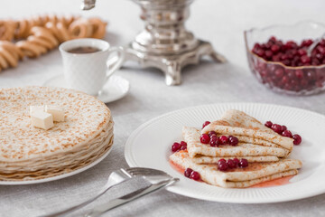 Russian traditions. Russian holiday Maslenitsa. Still life with a cup of tea, a stack of pancakes with northern cranberries, cubes of butter and samovars on the table.