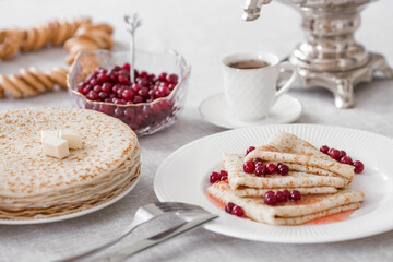 Russian traditions. Russian holiday Maslenitsa. Still life with a cup of tea, a stack of pancakes with northern cranberries, cubes of butter and samovars on the table.
