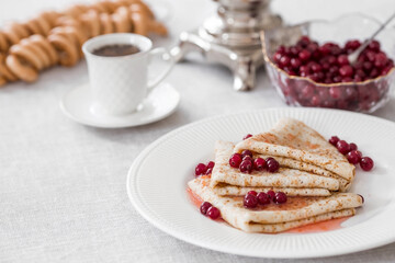 Russian traditions. Russian holiday Maslenitsa. Still life with a cup of tea, a stack of pancakes with northern cranberries, cubes of butter and samovars on the table.
