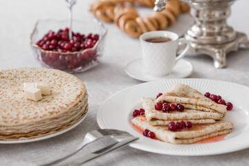 Russian traditions. Russian holiday Maslenitsa. Still life with a cup of tea, a stack of pancakes with northern cranberries, cubes of butter and samovars on the table.