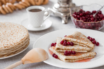 Russian traditions. Russian holiday Maslenitsa. Still life with a cup of tea, a stack of pancakes with northern cranberries, cubes of butter and samovars on the table.