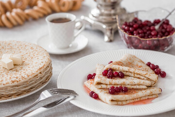 Russian traditions. Russian holiday Maslenitsa. Still life with a cup of tea, a stack of pancakes with northern cranberries, cubes of butter and samovars on the table.