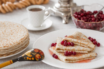 Russian traditions. Russian holiday Maslenitsa. Still life with a cup of tea, a stack of pancakes with northern cranberries, cubes of butter and samovars on the table.