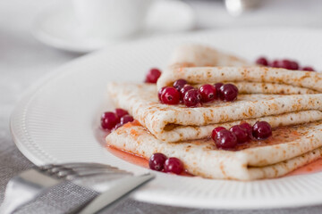 Russian traditions. Russian holiday Maslenitsa. Still life with a cup of tea, a stack of pancakes with northern cranberries, cubes of butter on the table.