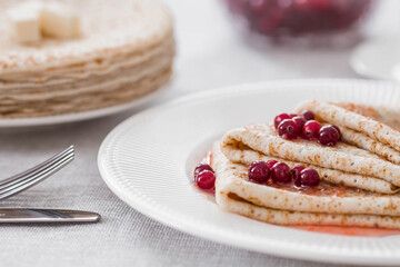 Russian traditions. Russian holiday Maslenitsa. Still life with a cup of tea, a stack of pancakes with northern cranberries, cubes of butter on the table.
