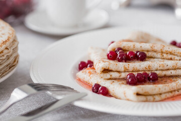 Russian traditions. Russian holiday Maslenitsa. Still life with a cup of tea, a stack of pancakes with northern cranberries, cubes of butter on the table.
