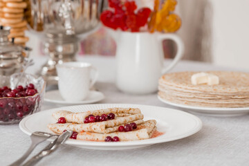 Russian traditions. Russian holiday Maslenitsa. Still life with a cup of tea, a stack of pancakes with northern cranberries, cubes of butter and samovars on the table.