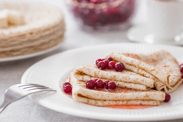 Russian traditions. Russian holiday Maslenitsa. Still life with a cup of tea, a stack of pancakes with northern cranberries, cubes of butter on the table.