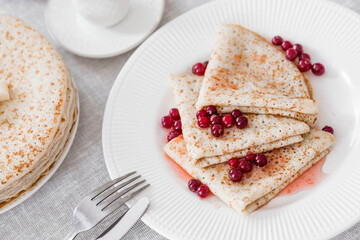 Russian traditions. Russian holiday Maslenitsa. Still life with a cup of tea, a stack of pancakes with northern cranberries, cubes of butter on the table.