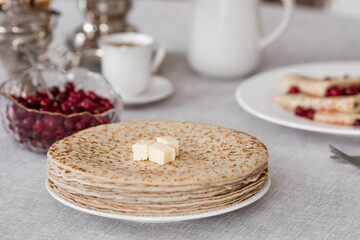 Russian traditions. Russian holiday Maslenitsa. Still life with a cup of tea, a stack of pancakes with northern cranberries, cubes of butter and samovars on the table.