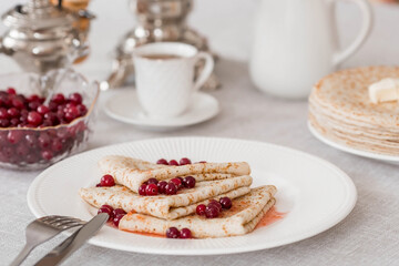 Russian traditions. Russian holiday Maslenitsa. Still life with a cup of tea, a stack of pancakes with northern cranberries, cubes of butter and samovars on the table.