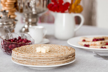 Russian traditions. Russian holiday Maslenitsa. Still life with a cup of tea, a stack of pancakes with northern cranberries, cubes of butter and samovars on the table.