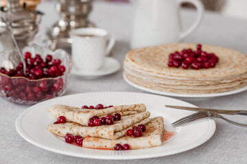 Russian traditions. Russian holiday Maslenitsa. Still life with a cup of tea, a stack of pancakes with northern cranberries, cubes of butter and samovars on the table.