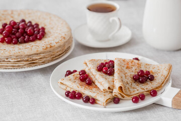 Russian traditions. Russian holiday Maslenitsa. Still life with a cup of tea, a stack of pancakes with northern cranberries, cubes of butter on the table.