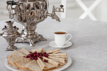 Russian traditions. Russian holiday Maslenitsa. Still life with a cup of tea, a stack of pancakes with northern cranberries, cubes of butter and samovars on the table.