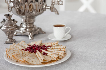 Russian traditions. Russian holiday Maslenitsa. Still life with a cup of tea, a stack of pancakes with northern cranberries, cubes of butter and samovars on the table.