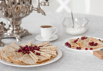 Russian traditions. Russian holiday Maslenitsa. Still life with a cup of tea, a stack of pancakes with northern cranberries, cubes of butter and samovars on the table.
