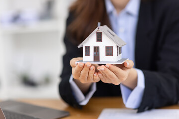 Wooden toy house with real estate agent Asian business woman signs a purchase contract mortgagefor...