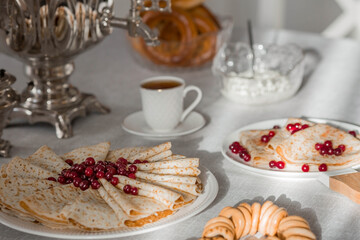 Russian traditions. Russian holiday Maslenitsa. Still life with a cup of tea, a stack of pancakes with northern cranberries, cubes of butter and samovars on the table.