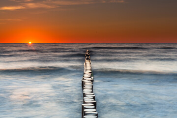 Sunset on the Baltic Sea in Rowy, Poland. Landscape with waterbreak in the sea under the sky at...