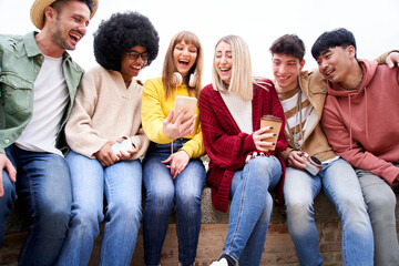 Group of multicultural young teenagers sitting together looking phone and laughing out loud....