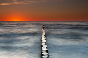 Colorful sunset on the Baltic Sea in Rowy, Poland. Landscape with waterbreak in the sea under the...