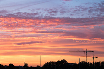 sunset over the city with the silhouettes of some construction cranes