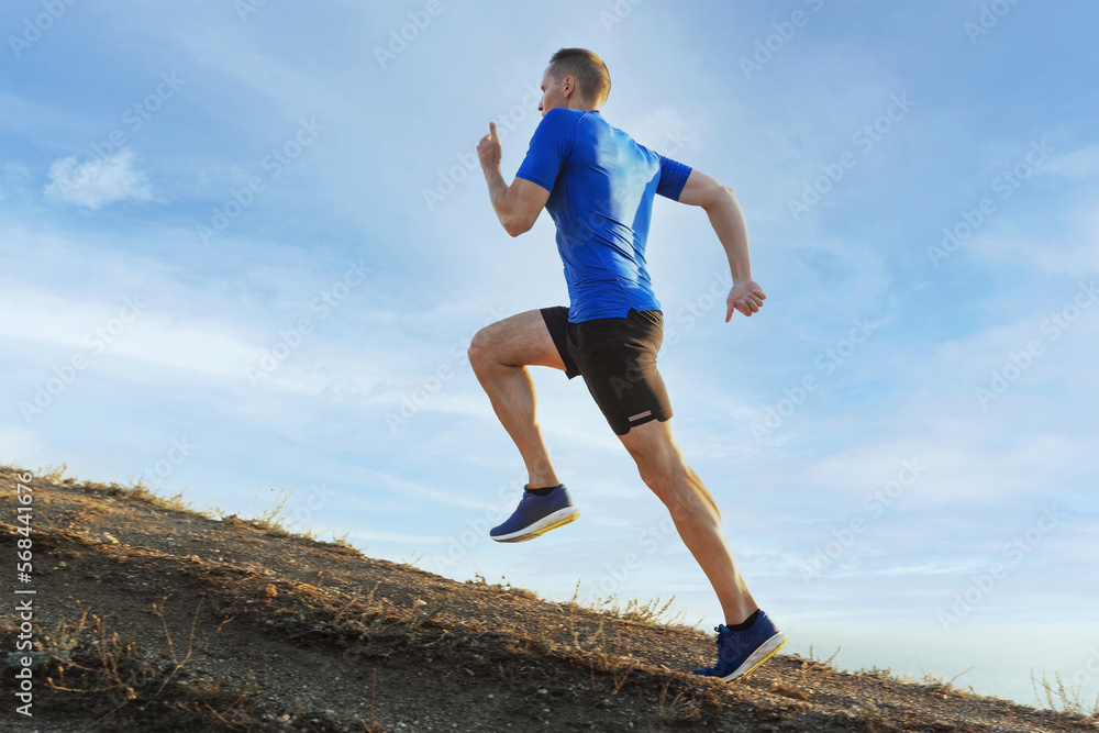 Wall mural man athlete runner running uphill in background blue sky