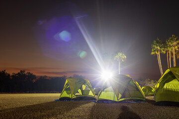 A view of a green canvas camping tent illuminated by floodlights set up on the lawn.