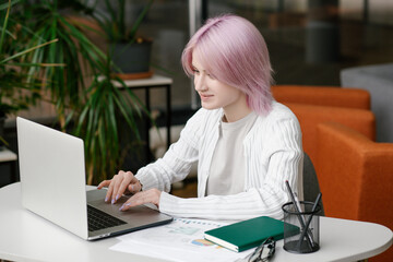 Beautiful young woman with short pink hair working laptop at modern office. Working on design, data analysis, plan strategy