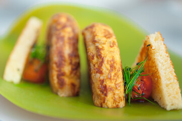 Close-up of Spanish Omelette with two slices of toast, cherry tomatoes, and chives. Breakfast meal of fried potatoes and eggs on a neon green plate. Modern food plating. Horizontal brunch background.