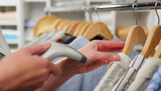 Fashionable clothes, Stylish woman Confidently scans a barcode with a scanner. Hanger with clothes, In slow motion Sales assistant Going through hangers with clothes in a warehouse, climate change
