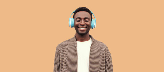 Portrait of happy smiling african man listening to music in wireless headphones wearing knitted...