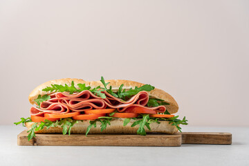 Italian style sandwich with arugula, mortadella ham and tomatoes. Baguette toast on wooden board on...