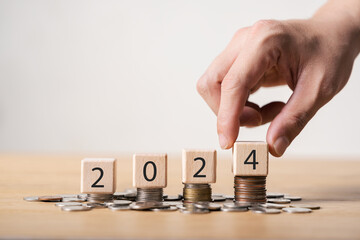 2024 new year goals planning concept, wooden cubes on stack of coins, positive indicator 2024,...