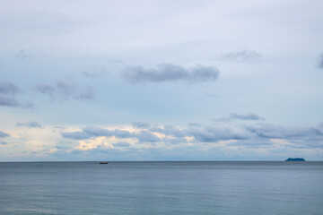 Blue tropical seascape with lone long tail boat and a distant island.
