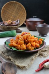 spicy potatoes on a clay plate against a backdrop of woven bamboo containers and clay pots