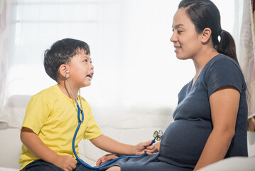 Asian young boy wearing stethoscope to act as doctor hear the baby in the mother's womb.,pregnant woman and young child, the idea of family love,