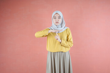 Beautiful Asian woman in yellow shirt and hijab silent instruction on brown background 