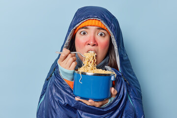 Hungry Asian woman with red skin after spending much time on frosty weather eats noodle wrapped in...
