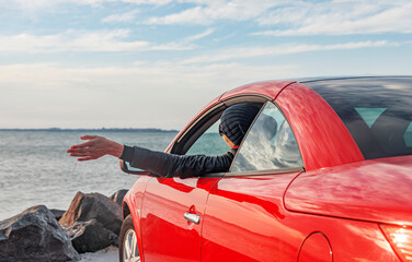 Fototapeta na wymiar Woman in red car with open roof at background of sea water. Travel, freedom and holidays concept.