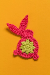 Cute Easter crochet bunny on a yellow background. Pink bunny with floral pattern. Top view. Copy space.