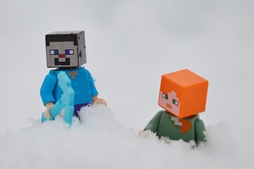 Naklejka premium LEGO Minecraft figures of Steve and Alex climbing in deep snow, winter cloudy sunshine.