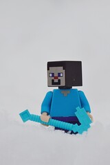 Fototapeta premium LEGO Minecraft figure of main character Steve standing with his diamond pickaxe in deep snow.